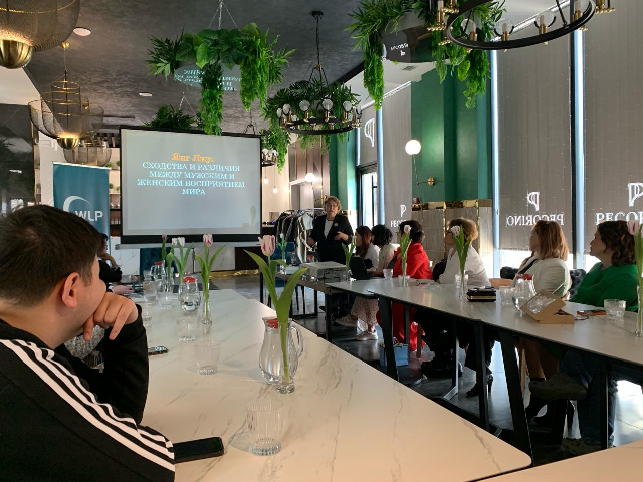 A leadership and gender justice training held by SWRC with people seated around a conference room table and a screen with Russian text in the center