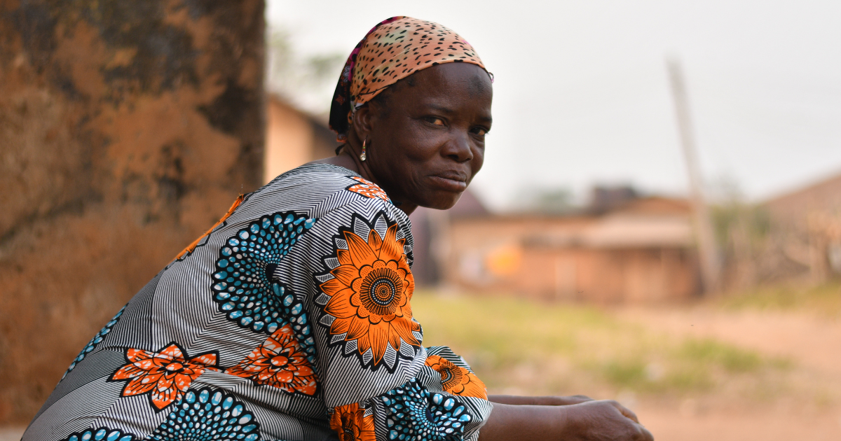 Nigerian woman sits outsides of her home. 